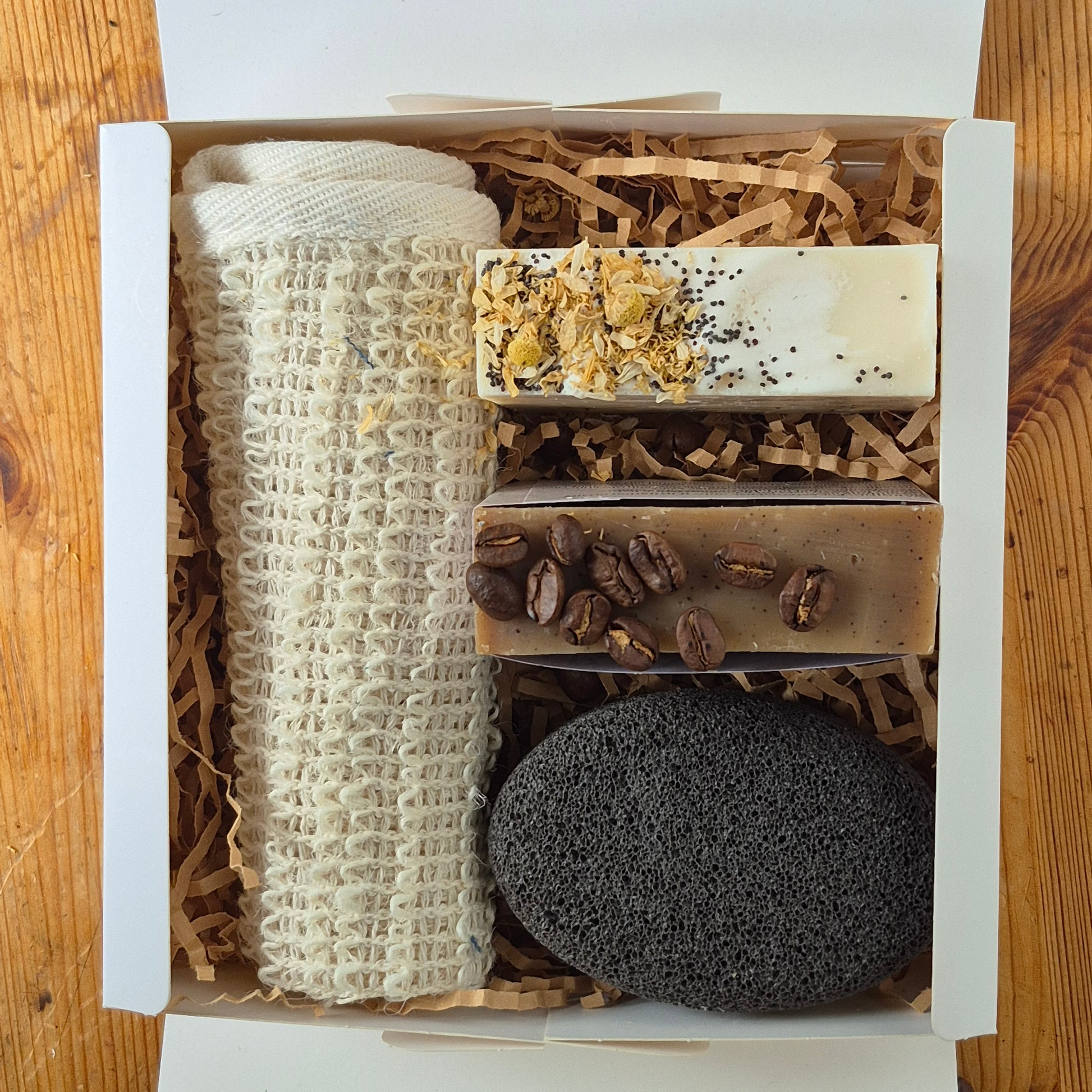 Set of natural products including soap, coffee beans, and a pumice stone in a box on a wooden surface.