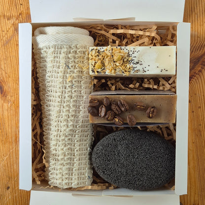 Set of natural products including soap, coffee beans, and a pumice stone in a box on a wooden surface.